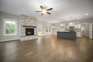 Spacious modern living area at Shirley Commons with fireplace, wood floors, ceiling fans, and open kitchen with island.