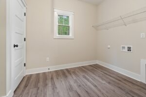 Empty laundry room with beige walls, wood floor, window, and wire shelf—common in new homes in Richmond VA.