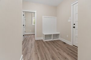A bright entryway with wood flooring, perfect for new homes in Richmond VA, features a white bench and black hardware.