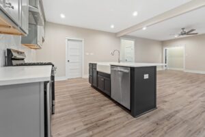 Modern kitchen at Shirley Commons with gray cabinets, farmhouse sink, island, and stainless steel appliances on wood flooring.