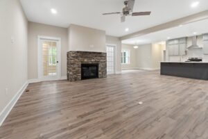 Spacious open living area with wood floors, stone fireplace, and view of modern kitchen in new homes in Richmond VA.