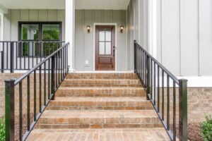 Brick steps with black railings lead to a wooden door on a modern gray-sided house—perfect for new homes in Richmond VA.