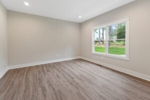 Empty room with light gray walls, wood flooring, and large window in new homes in Richmond VA overlooking a grassy yard.