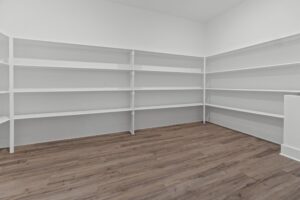 Empty white shelves in a walk-in pantry with wood flooring in new homes in Richmond, VA, and bright lighting.