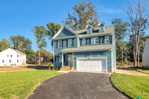 Blue two-story house with attached garage on Lot 29, Poplar Village, featuring a driveway and green lawn.