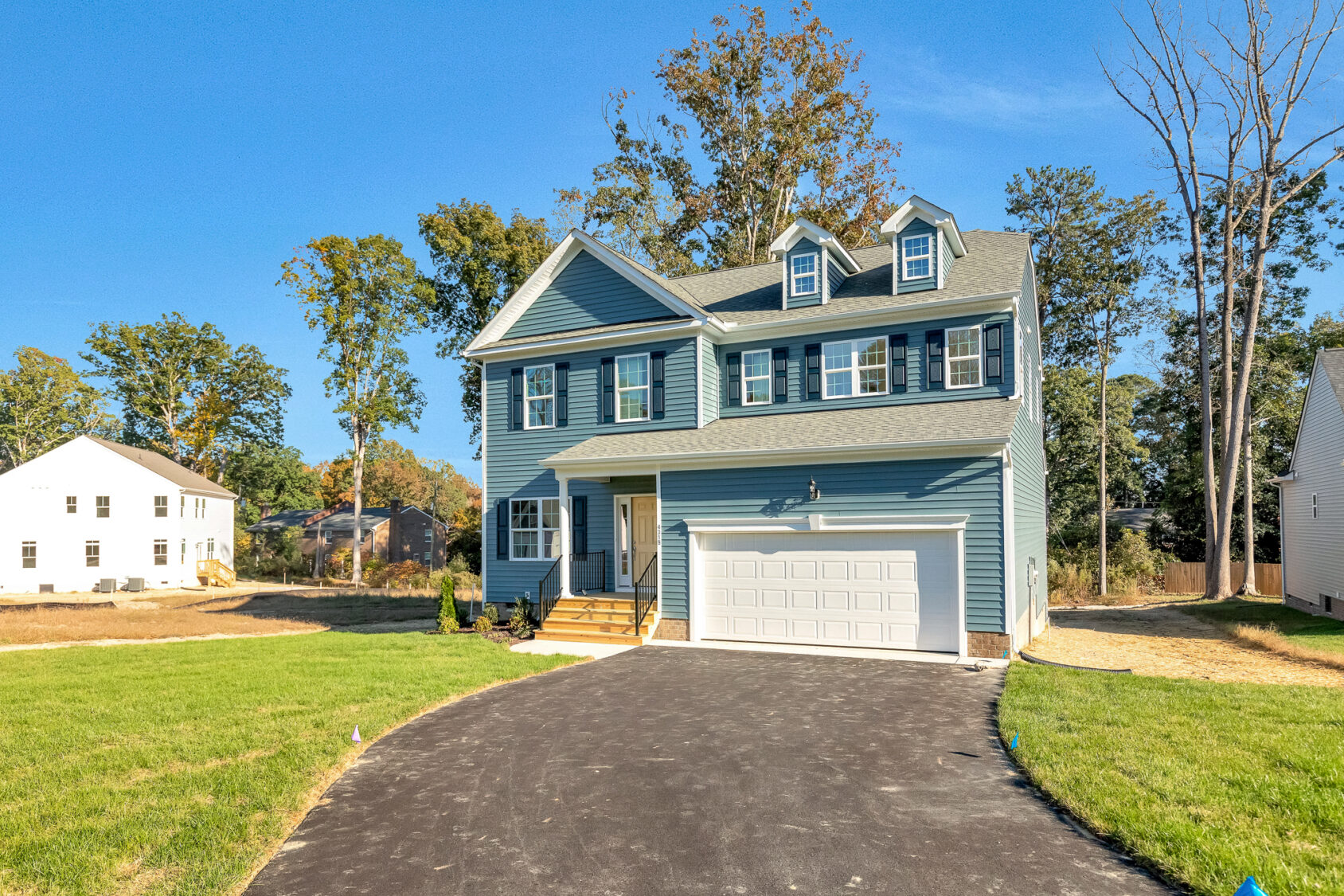 A two-story blue house in Poplar Village with a white garage and shuttered windows, set on Lot 29’s grassy lawn.