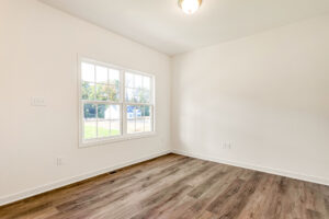 Empty room in Poplar Village, Lot 29, with light walls, large window, wood flooring, and ceiling light fixture.