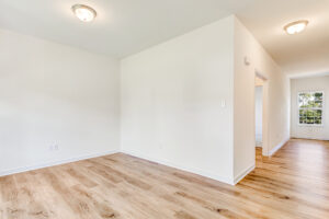 Bright, empty room in Poplar Village with white walls, wood flooring, ceiling lights, and a distant window.