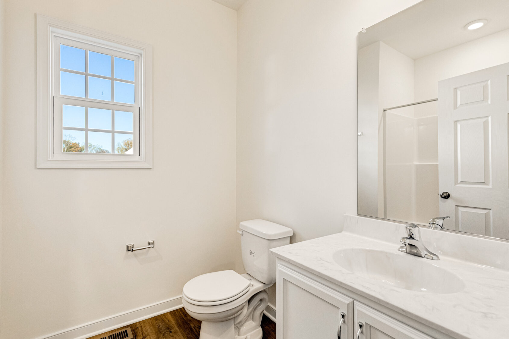 Bright bathroom in Poplar Village, Lot 29, featuring a white toilet, sink, mirror, shower stall, and natural light.