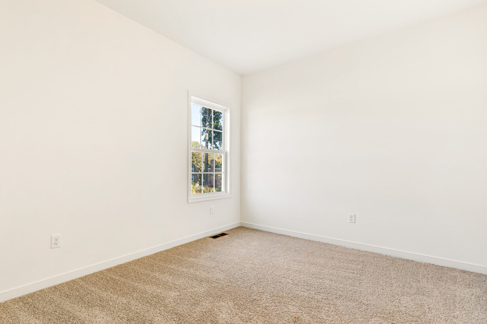 Empty room in Poplar Village with beige carpet, white walls, and a window filling Lot 29 with natural light.