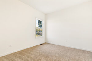 Empty room in Poplar Village with beige carpet, white walls, and a window filling Lot 29 with natural light.