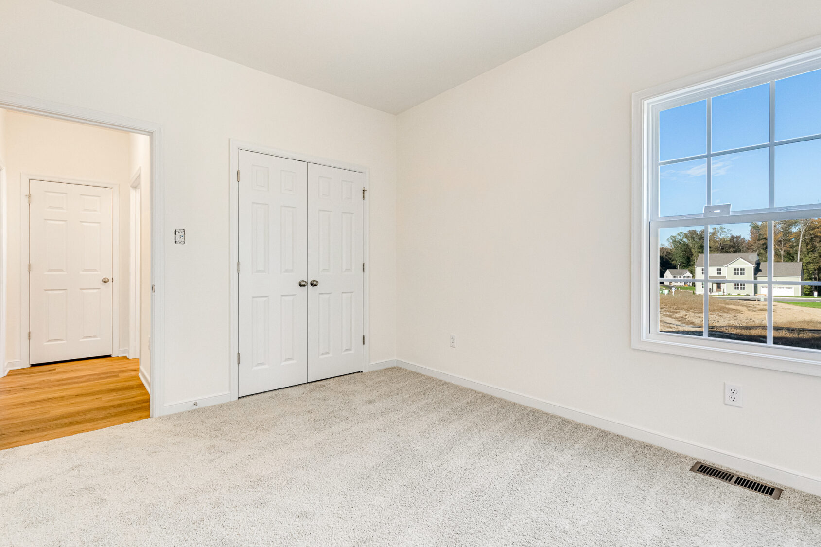 Bright, empty room with light carpet, white walls, double closet in Poplar Village Lot 29, window overlooks houses.