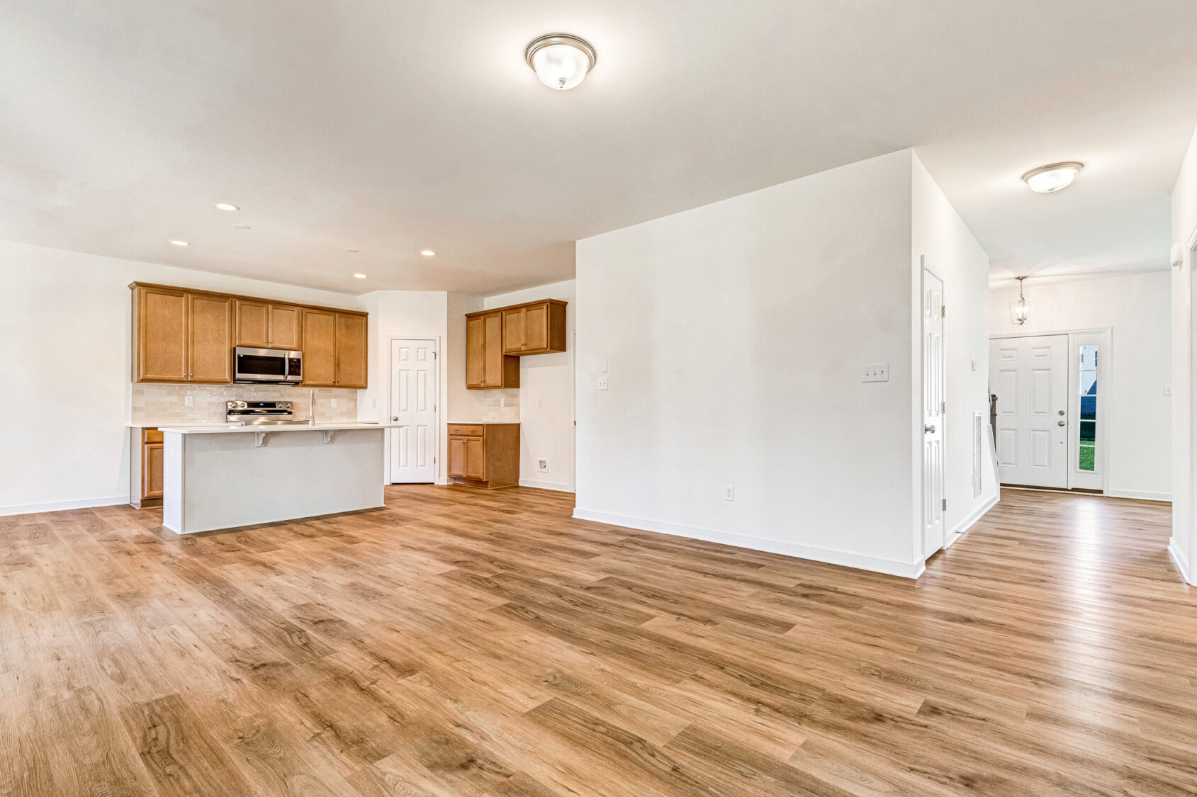 Open-plan kitchen and living area with wood flooring in Poplar Village, leading to a bright front entryway.