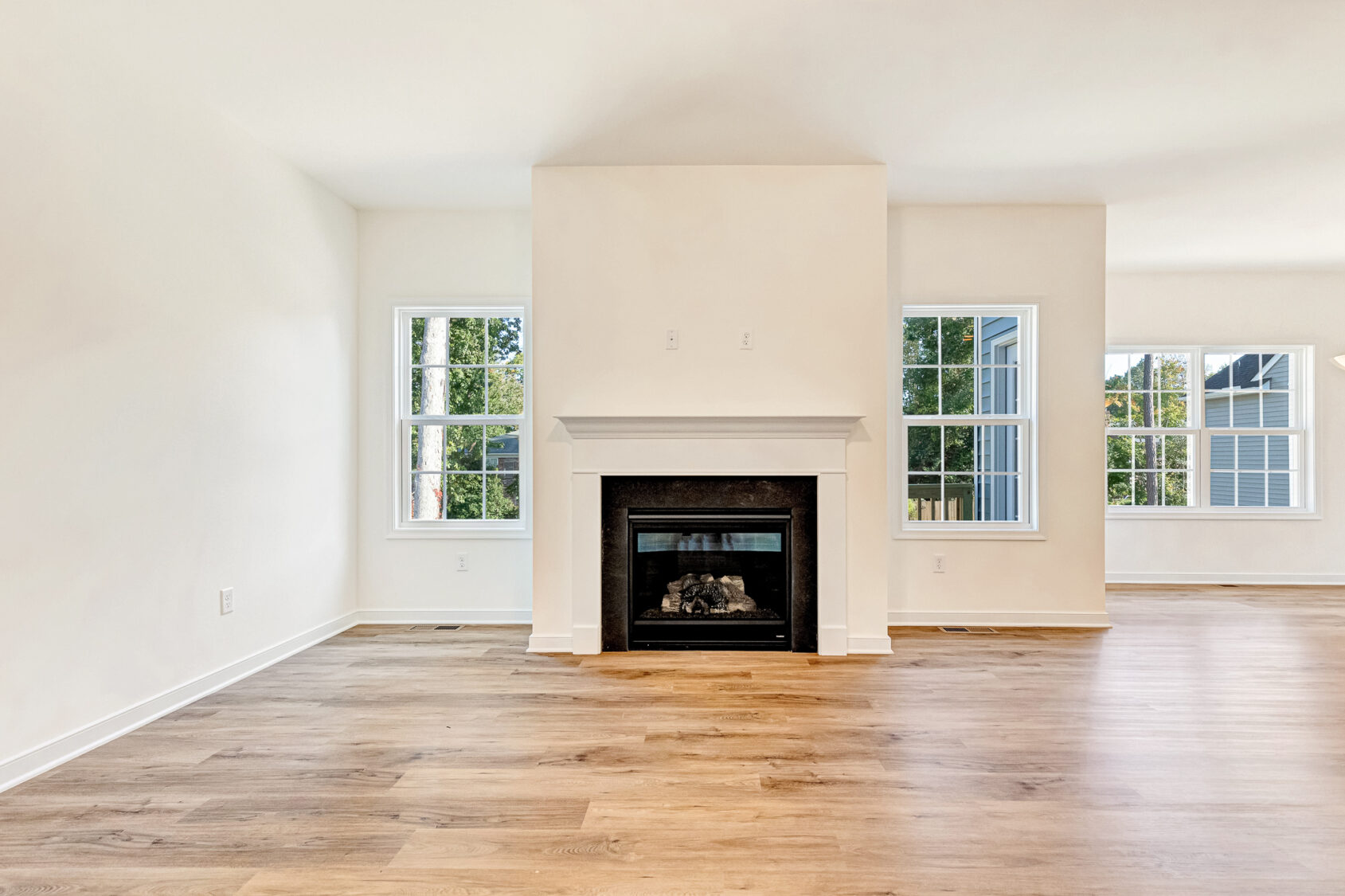 Bright empty living room in Lot 29, Poplar Village, with large windows, light wood floors, and a white fireplace.