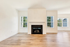Bright empty living room in Lot 29, Poplar Village, with large windows, light wood floors, and a white fireplace.