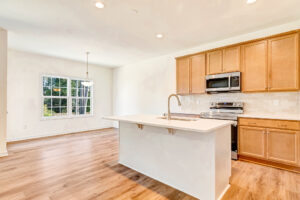 Bright kitchen in Poplar Village with wood cabinets, stainless appliances, island, and window overlooking trees.