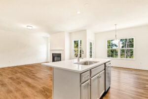 Bright modern kitchen in Lot 29, Poplar Village, with white island, wood floors, and large windows open to living area.
