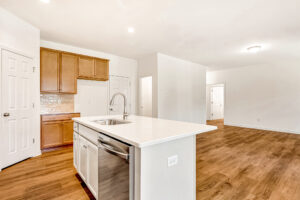 Modern kitchen in Poplar Village Lot 29 with wood floors, white island, and stainless steel dishwasher.