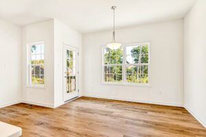 Bright, empty room with wood flooring in Lot 29, Poplar Village—white walls, large windows, and a hanging light fixture.