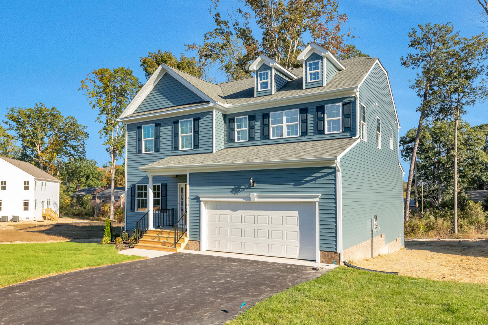 Two-story blue house with white trim in Poplar Village, Lot 29, featuring a double garage and blacktop driveway.