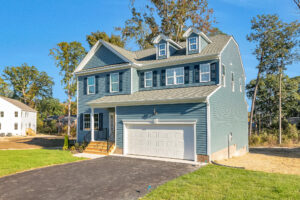 Two-story blue house with white trim in Poplar Village, Lot 29, featuring a double garage and blacktop driveway.