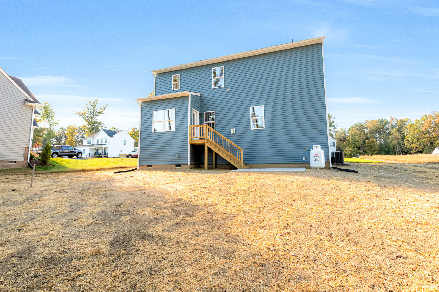 Blue two-story house on Lot 29 in Poplar Village with wooden stairs leading to a backyard with dry grass and distant trees.