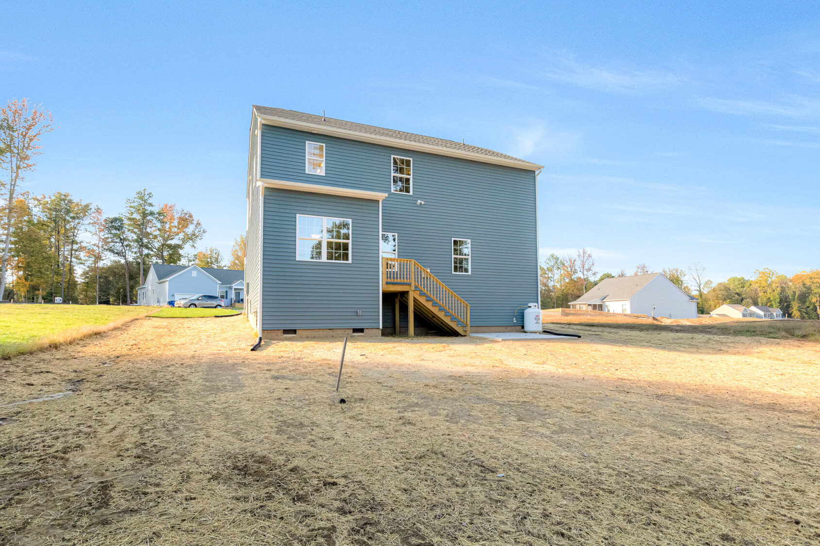 Two-story house with gray siding in Poplar Village, wooden stairs, and dry backyard under a clear blue sky.
