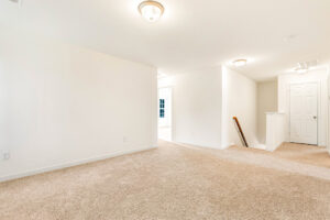 Bright, empty carpeted room in Poplar Village with white walls, ceiling lights, and a hallway to a closed door.