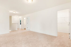 Empty, carpeted room in Poplar Village's Lot 29 with white walls, ceiling lights, multiple doors, and a walk-in closet.