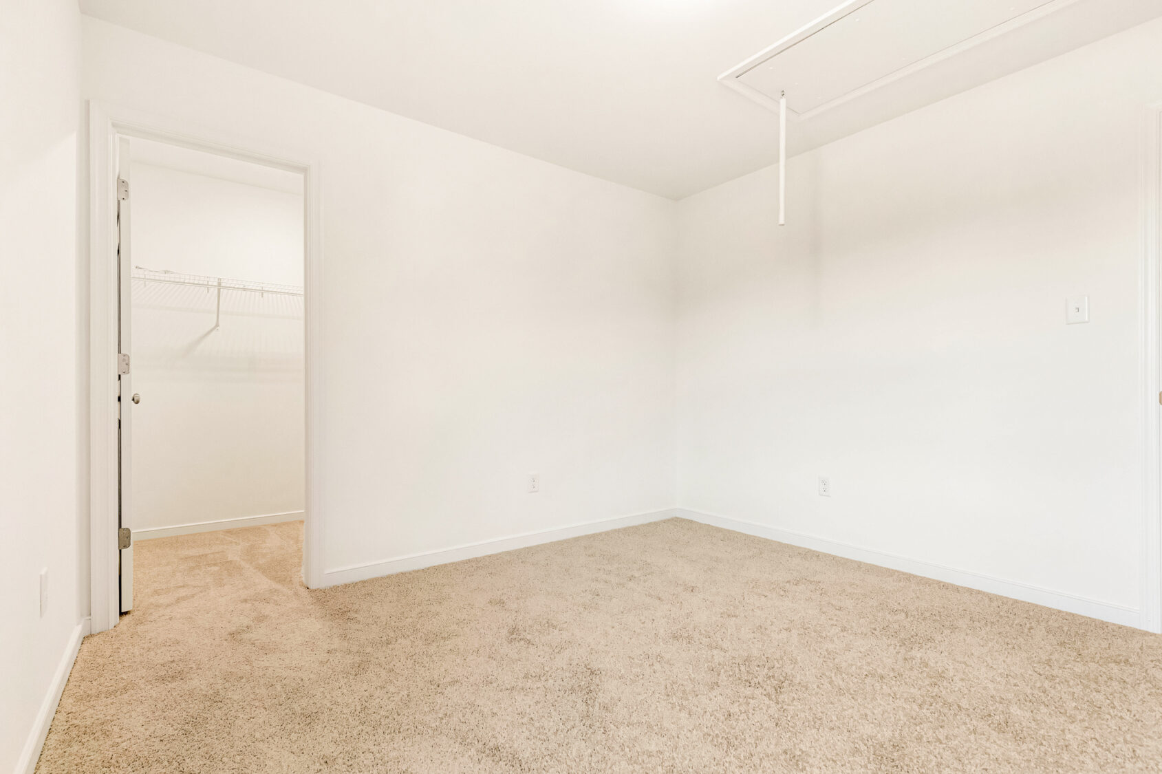 Empty carpeted room in Poplar Village, Lot 29, with white walls, closet door, and ceiling attic access panel.
