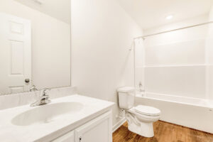 Bright, clean bathroom in Lot 29, Poplar Village, with white walls, a sink, toilet, and bathtub with shower curtain rod.
