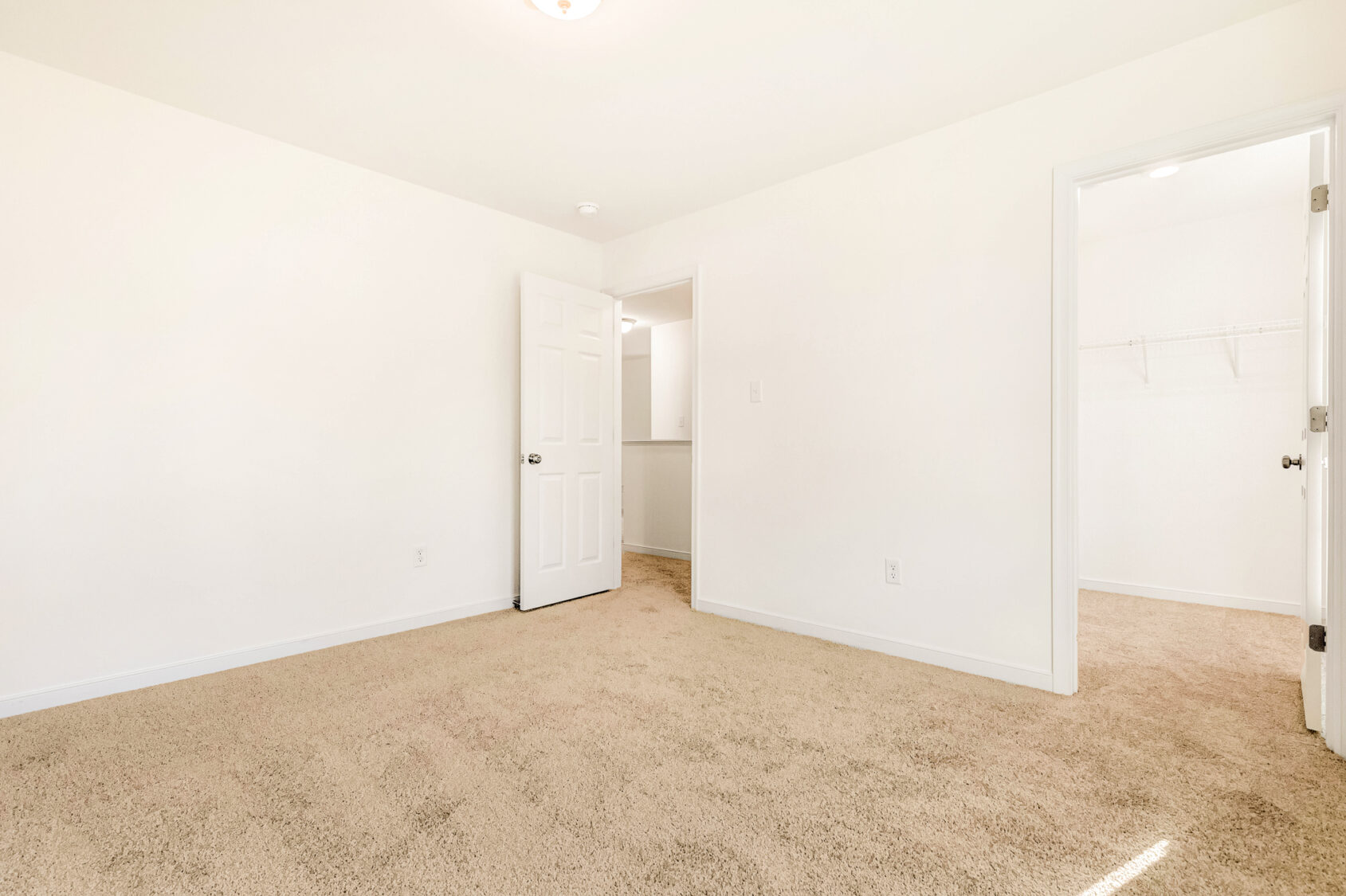Empty carpeted room in Poplar Village with white walls, open door, and walk-in closet with shelves—Lot 29.