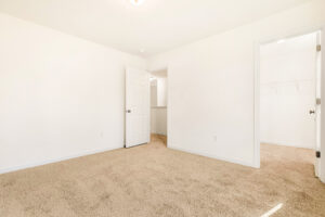 Empty carpeted room in Poplar Village with white walls, open door, and walk-in closet with shelves—Lot 29.