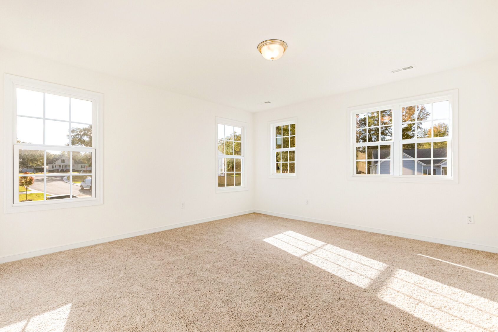 Bright, empty room in Poplar Village, Lot 29, with beige carpet, white walls, and large sunlit windows.