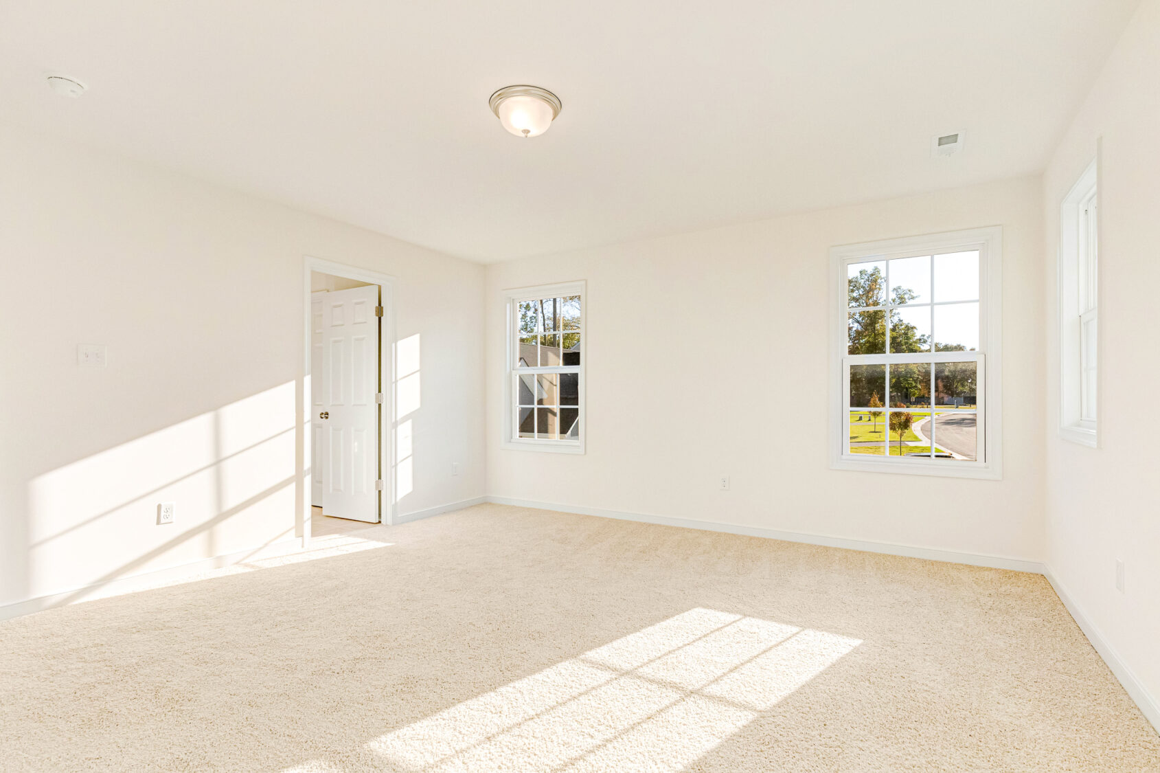 Bright, empty room in Poplar Village's Lot 29 with beige carpet, white walls, and sunlight streaming through windows.
