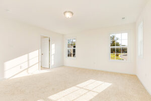 Bright, empty room in Poplar Village's Lot 29 with beige carpet, white walls, and sunlight streaming through windows.