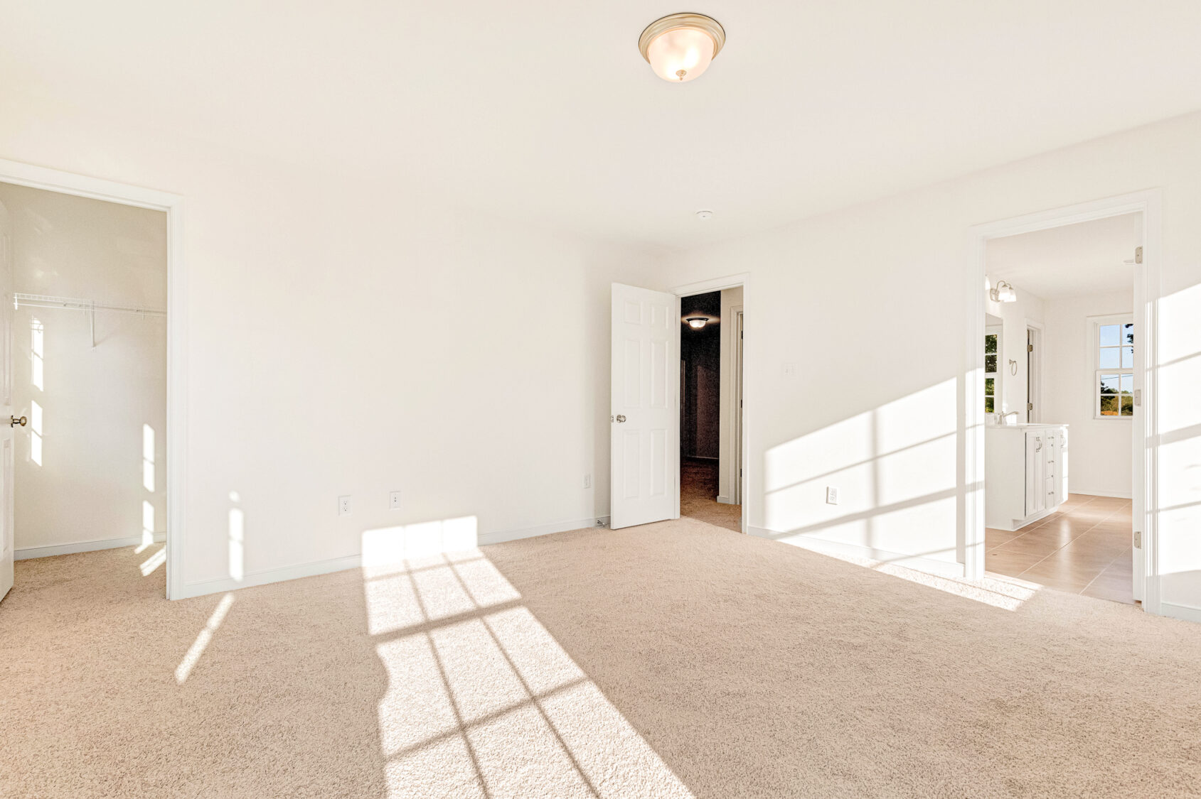 Bright, empty Poplar Village bedroom with beige carpet, white walls, and sunlight streaming through large windows.