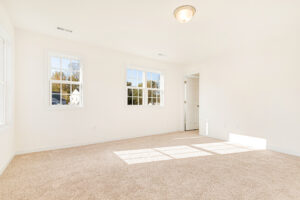 Bright, empty carpeted room in Poplar Village with white walls, three windows, and a ceiling light fixture.