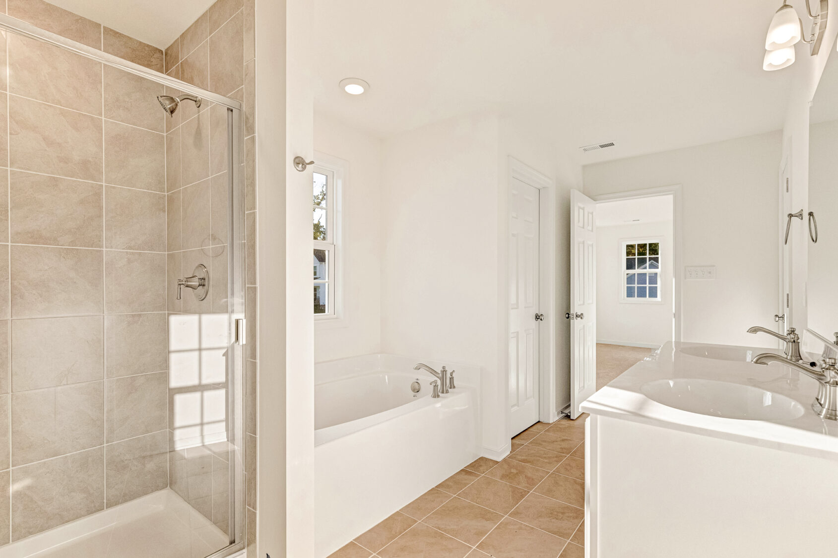 Bright bathroom in Poplar Village Lot 29 with glass shower, bathtub, double sinks, and beige tile flooring.