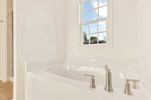 White bathtub with silver fixtures beneath a window in bright Poplar Village Lot 29 bathroom with sky views.