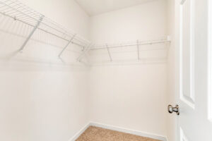 Empty walk-in closet in Poplar Village Lot 29 with white wire shelves, white walls, and beige carpet flooring.