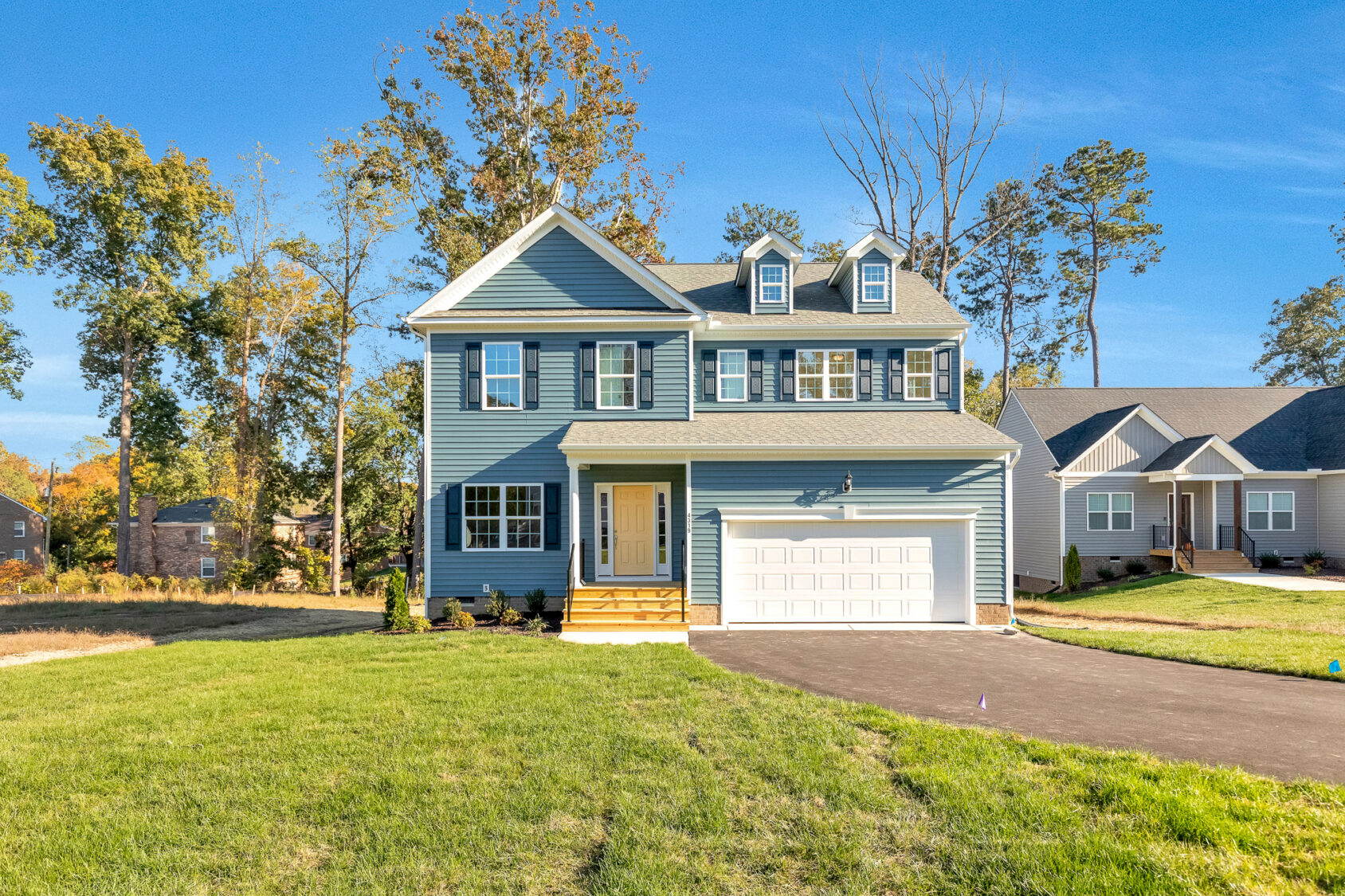 Two-story blue house with white trim and garage on sunny, grassy Lot 29 in Poplar Village.