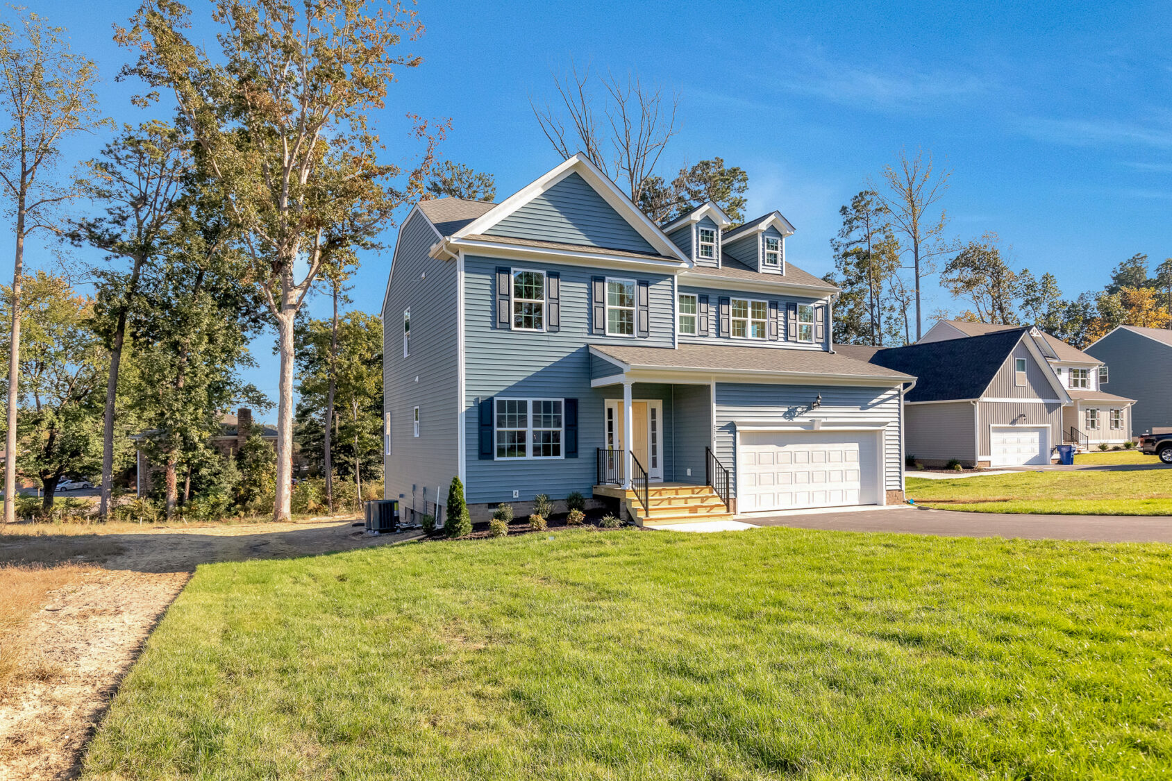 Charming two-story blue home on Lot 29 in Poplar Village, featuring white trim, garage, and lush green lawn.
