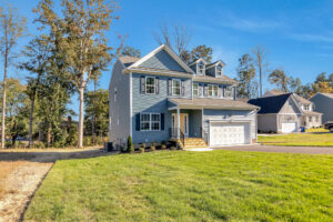Charming two-story blue home on Lot 29 in Poplar Village, featuring white trim, garage, and lush green lawn.