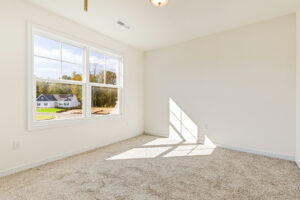 Bright empty room in Poplar Village, with beige carpet, large window, and sunlight streaming onto the floor.