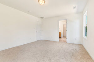 Empty carpeted room with white walls in Poplar Village Lot 23; includes window, closet, and doorway to a bathroom.
