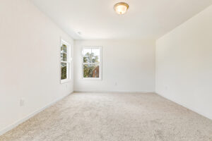 Bright, empty room in Poplar Village's Lot 23 with beige carpet, white walls, two windows, and a ceiling light fixture.