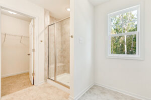 Bright bathroom with a glass shower, closet entrance, and window overlooking trees in Poplar Village Lot 23.