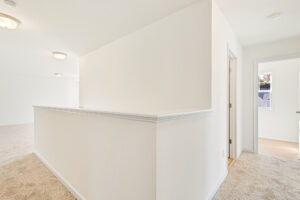 Bright hallway in Poplar Village with beige carpet, white walls, and a doorway to Lot 23’s hardwood-floored room with window.