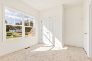 Bright, empty room with beige carpet in Poplar Village, double closet doors, and large window overlooking Lot 23.